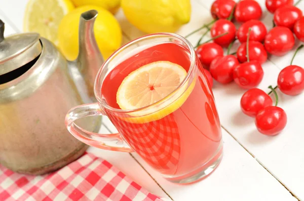 Фруктовый вишневый чай с ломтиком лимона в кружке, старый чайник и вишни — стоковое фото