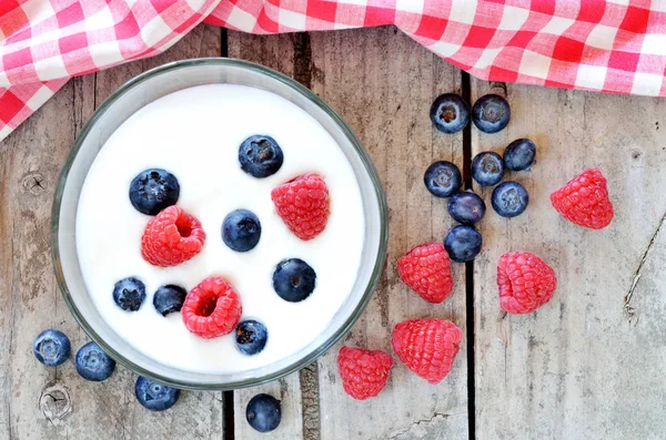 Weißer Joghurt in einer Schüssel mit Blaubeeren und Himbeeren auf Holztisch — Stockfoto