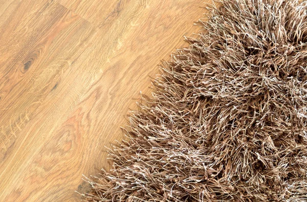 Коричневый лохматый ковер на коричневом деревянном полу — стоковое фото