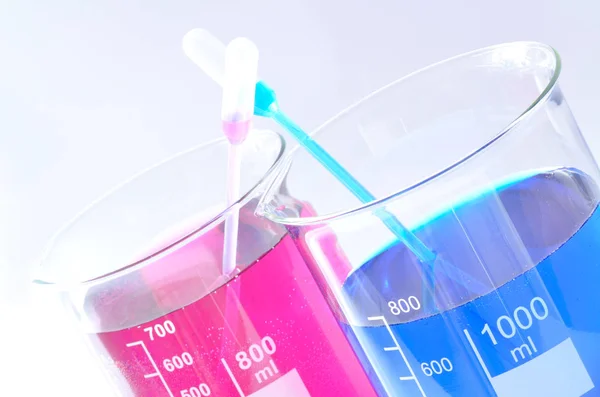 Béquer químico com produtos químicos azuis e vermelhos dissolvidos em água — Fotografia de Stock
