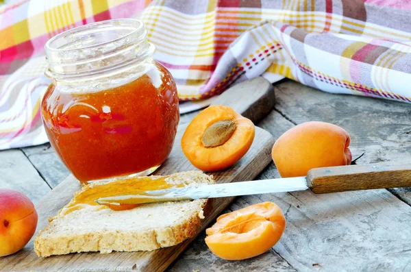 Jar of apricot jam and fresh apricots on wooden table — Stock Photo, Image