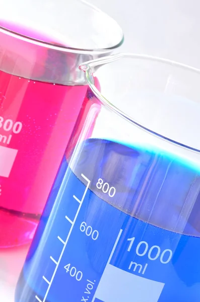 Becher chimici con sostanze chimiche blu e rosse disciolte in acqua — Foto Stock