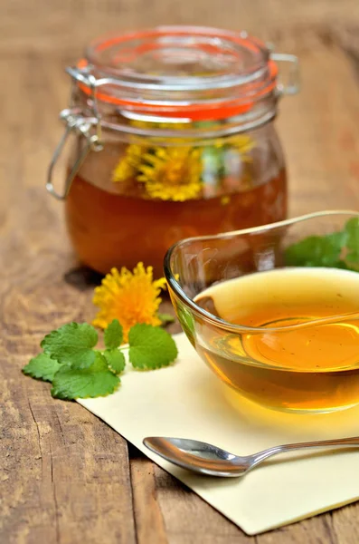 Close-up of dandelion honey in a glass bowl and dandelion head around, full jar in background - vertical photo — Stock Photo, Image