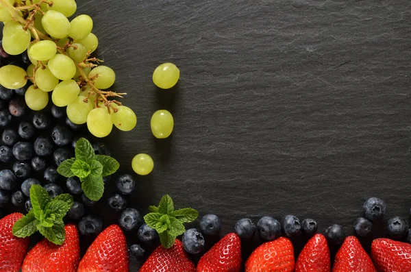 Fresas, arándanos, uvas y hojas de menta fresca en una losa de pizarra vintage. Vista superior, copyspace . — Foto de Stock