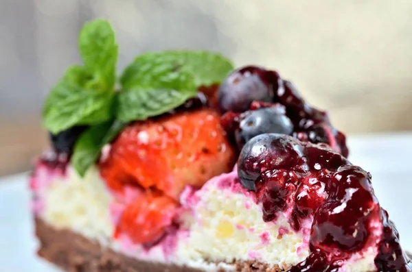 Close-up of delicious fruit strawberry and blueberry cream cake glazed by cherry sauce and fresh mint leaves on decorative white plate. Low depth of field. — Stock Photo, Image