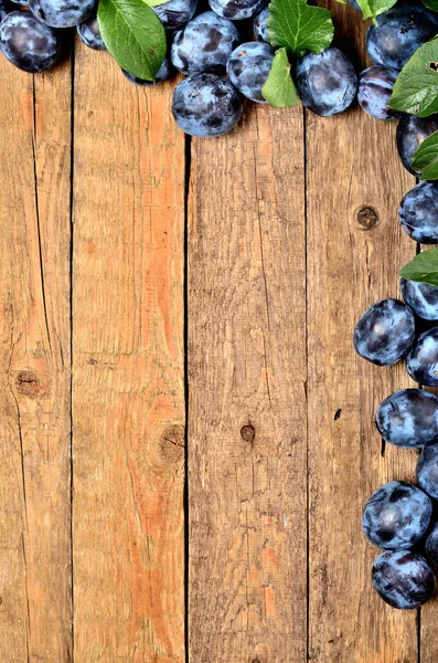 Fresh garden blue plums and leaves on rustic wooden background. VIew from above and copy space. — Stock Photo, Image