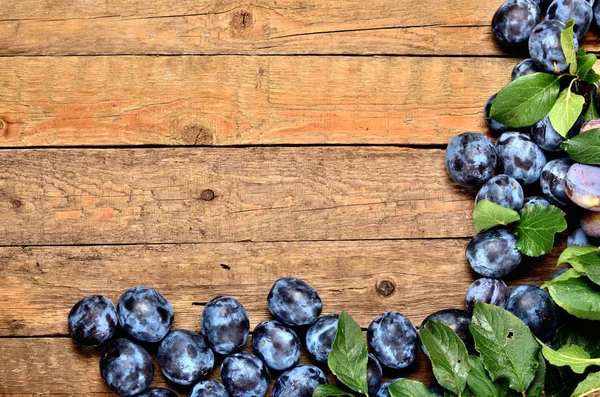 Fresh garden blue plums and leaves on rustic wooden background. Top view and copy space. — Stock Photo, Image