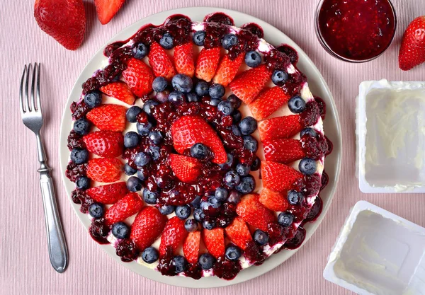 Köstliche Torte mit frischen Erdbeeren, Blaubeeren und Kirschmarmelade. Gabel, leere Schalen mit Quark und Schüssel mit Marmelade. Ansicht von oben. — Stockfoto