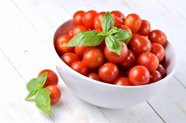Close-up of bowl of fresh cherry tomatoes and basil leaves on rustic wooden background. — Stock Photo, Image
