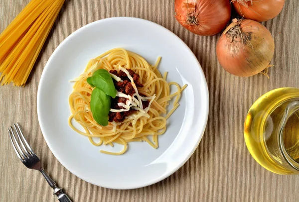 Spaghetti bolognese з пармезанським сиром і базилем. Італійська традиційна паста. Цибуля, олія і виделка на задньому плані. Краєвид. — стокове фото