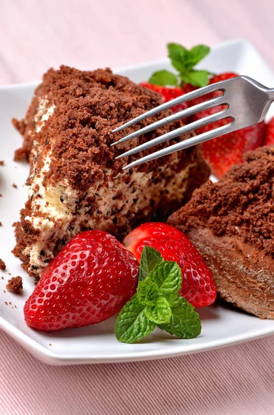 Gâteau maison au trou de taupe avec crème fouettée, banane, fraises et feuilles de menthe fraîche sur assiette décorative blanche. Gros plan avec fourchette . — Photo