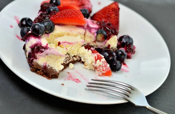 Gros plan de tarte au fromage à la fraise, à la myrtille et à la crème à moitié mangée dans une assiette avec cuillère — Photo