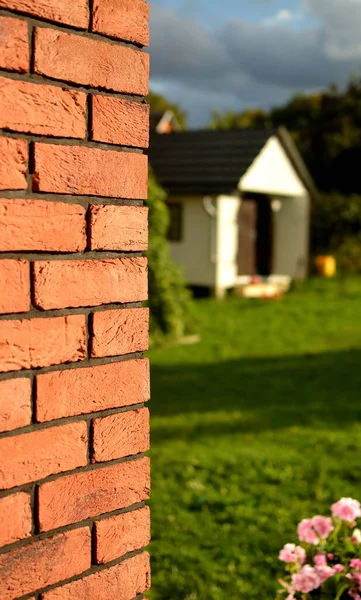 Brick wall in the foreground and summer garden with house in background low depth of field. Vertical photo. — Stock Photo, Image