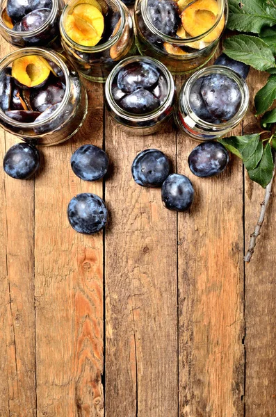 Fresh garden plums and jars on wooden background. Top view. Copy space for text. — Stock Photo, Image