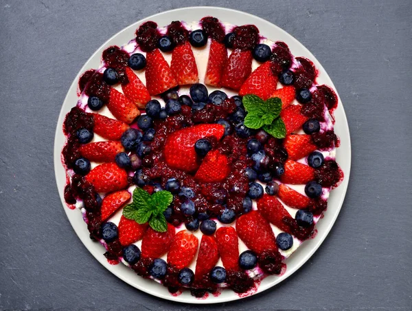 Köstlicher Kuchen mit frischen Erdbeeren, Blaubeeren, Kirschmarmelade und Minzblättern auf Schieferplatte. Ansicht von oben. — Stockfoto