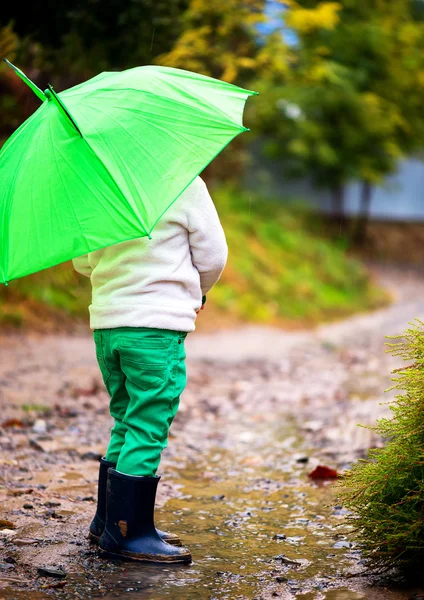 Flicka med paraply i regnet rinner genom pölar spelar i naturen — Stockfoto