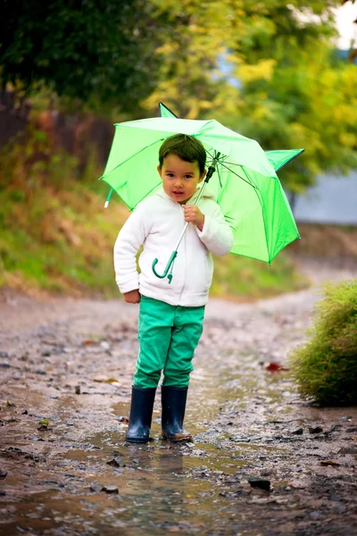 Flicka med paraply i regnet rinner genom pölar spelar i naturen — Stockfoto