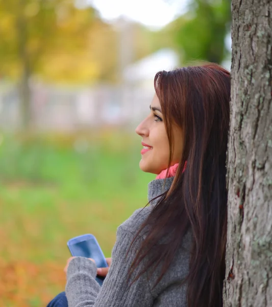 Hermosa chica de mensajería con teléfono en el parque de otoño — Foto de Stock