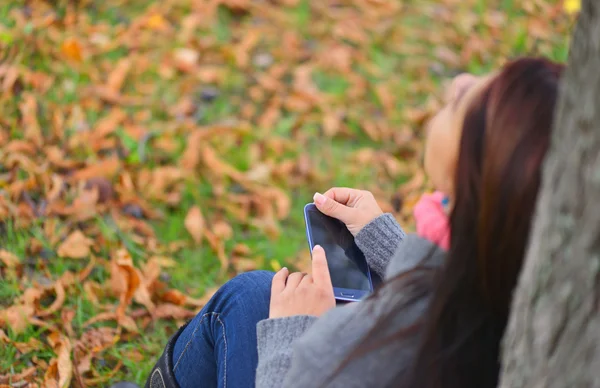 Beautiful girl messaging with phone in autumn park. Top view — Stock Photo, Image