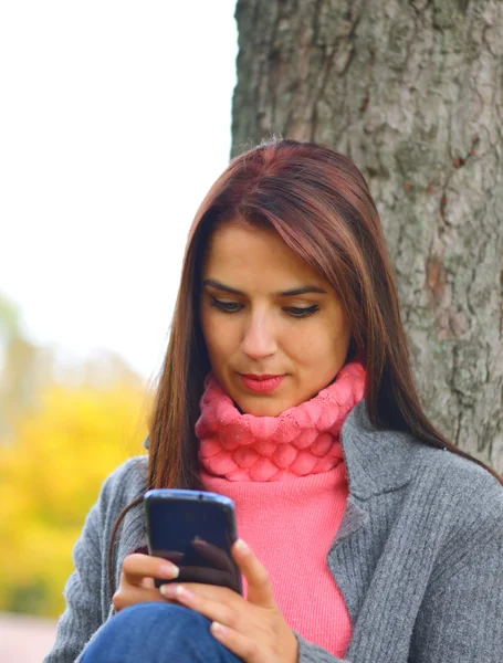 Beautiful girl messaging with phone in autumn park — Stock Photo, Image