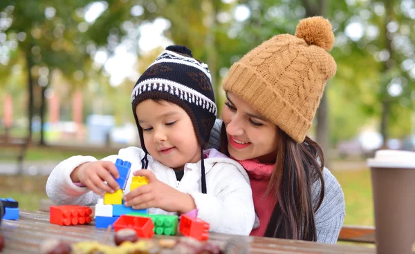 Mujer joven con su hijo jugando con bloques de plástico de colores al aire libre —  Fotos de Stock