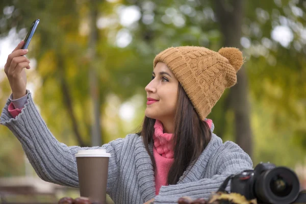 Mujer feliz chica tomando autofoto selfie con cámara de teléfono inteligente al aire libre en el parque de otoño en el banco — Foto de Stock