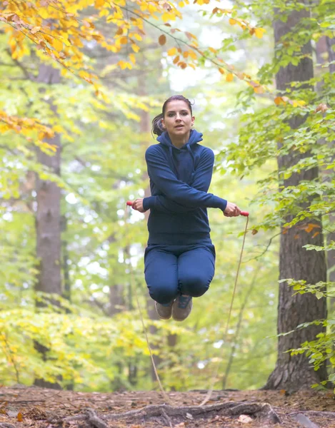 Young beautiful fitness woman skipping rope in forest, autumn colors — Stock Photo, Image