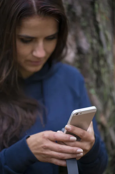 Žena držící mobilní telefon a sluchátka v ruce proti rozmazání podzim forrest pozadí — Stock fotografie