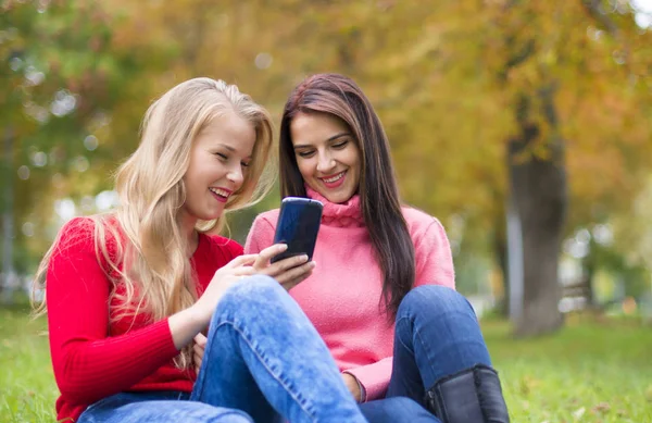 Dos chicas en el parque con un teléfono móvil — Foto de Stock