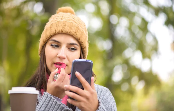 Žena dělat make-up, nanesení rtěnky při pohledu na telefon, jako v zrcadle — Stock fotografie