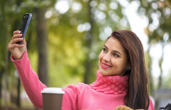 Teknik internet och lycka koncept. Kvinna glad tjej tar själv föreställer selfie med smartphone kamera utomhus i höst park på bänk — Stockfoto