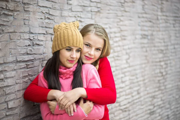 Due ragazze che si abbracciano e si divertono su uno sfondo di muro di mattoni — Foto Stock