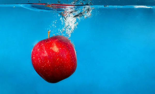 Rött äpple i vatten med stänk och droppar — Stockfoto