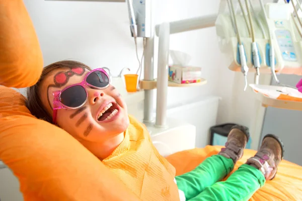 Pequena menina bonito sentado na cadeira no dentista com óculos de sol — Fotografia de Stock