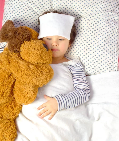 Meisje met een hoofdpijn in bed met teddybeer — Stockfoto