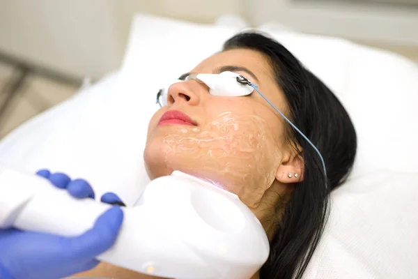 Vacker ung kvinna liggande på ett bord med protect glasögon på ögonen får en laser hudbehandling — Stockfoto