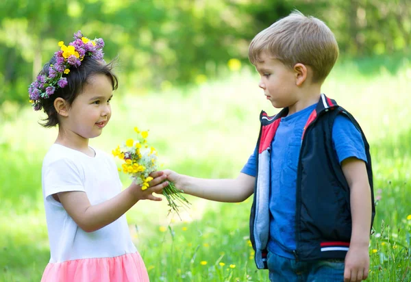 Kleiner Junge schenkt Blumen an ein kleines Mädchen — Stockfoto