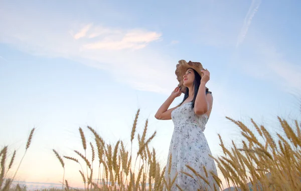 Hermosa mujer con sombrero de verano en el campo de trigo al atardecer — Foto de Stock