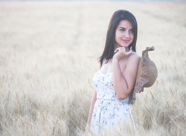 Hermosa mujer con sombrero de verano en el campo de trigo al atardecer — Foto de Stock