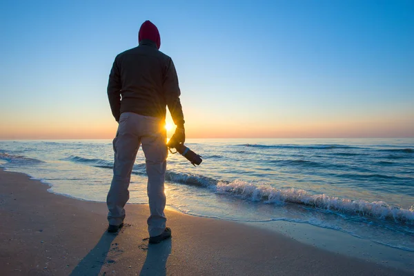 Man is het fotograferen van een zonsopgang tegen de achtergrond van de zee. — Stockfoto