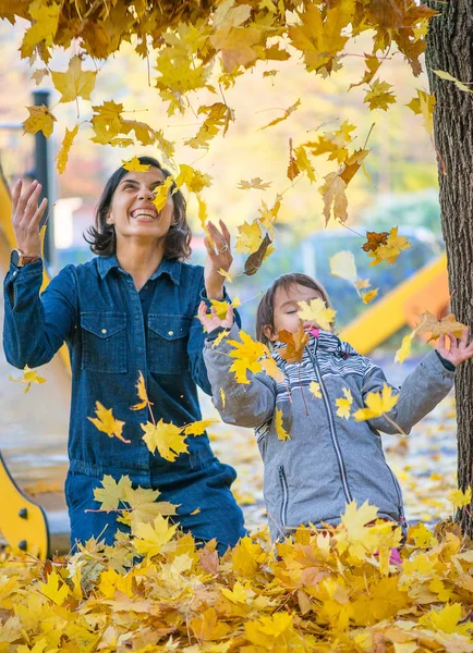 母亲和她的小 daugheter 有乐趣在公园与叶子 — 图库照片