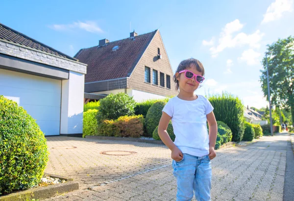 Liten flicka med händerna i fickorna leende på gatan — Stockfoto