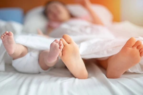 Tiny newborn\'s feet laying on the bed with elber sister or brother family sleep resting