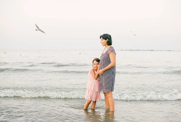 怀孕的母亲和女儿一起在海滩上享受阳光 — 图库照片