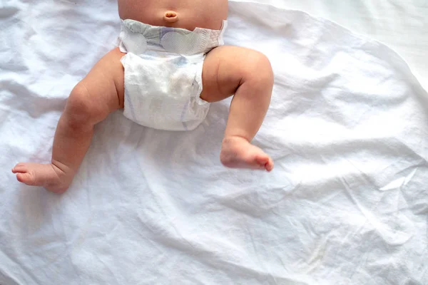 Baby legs and bottom in diaper on white bed background, top view, copy space