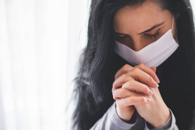 Cerrahi maskeli bir kadının portresi dua ediyor.