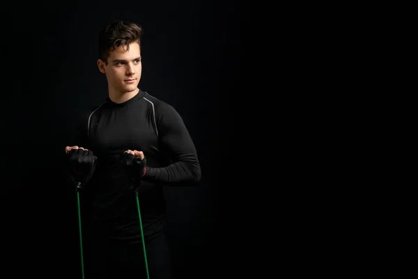 身穿黑色制服的年轻运动员站着 伸展着一条绿色的运动弹性带 — 图库照片