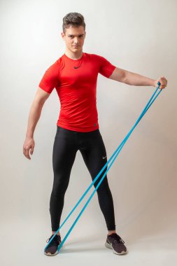 Beyaz arka planda izole edilmiş genç sporcu elastik bir bant takıyor.