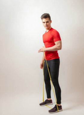 Beyaz arka planda izole edilmiş genç sporcu elastik bir bant takıyor.