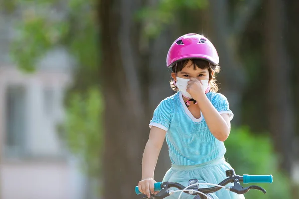 戴防护口罩的小女孩骑自行车 — 图库照片